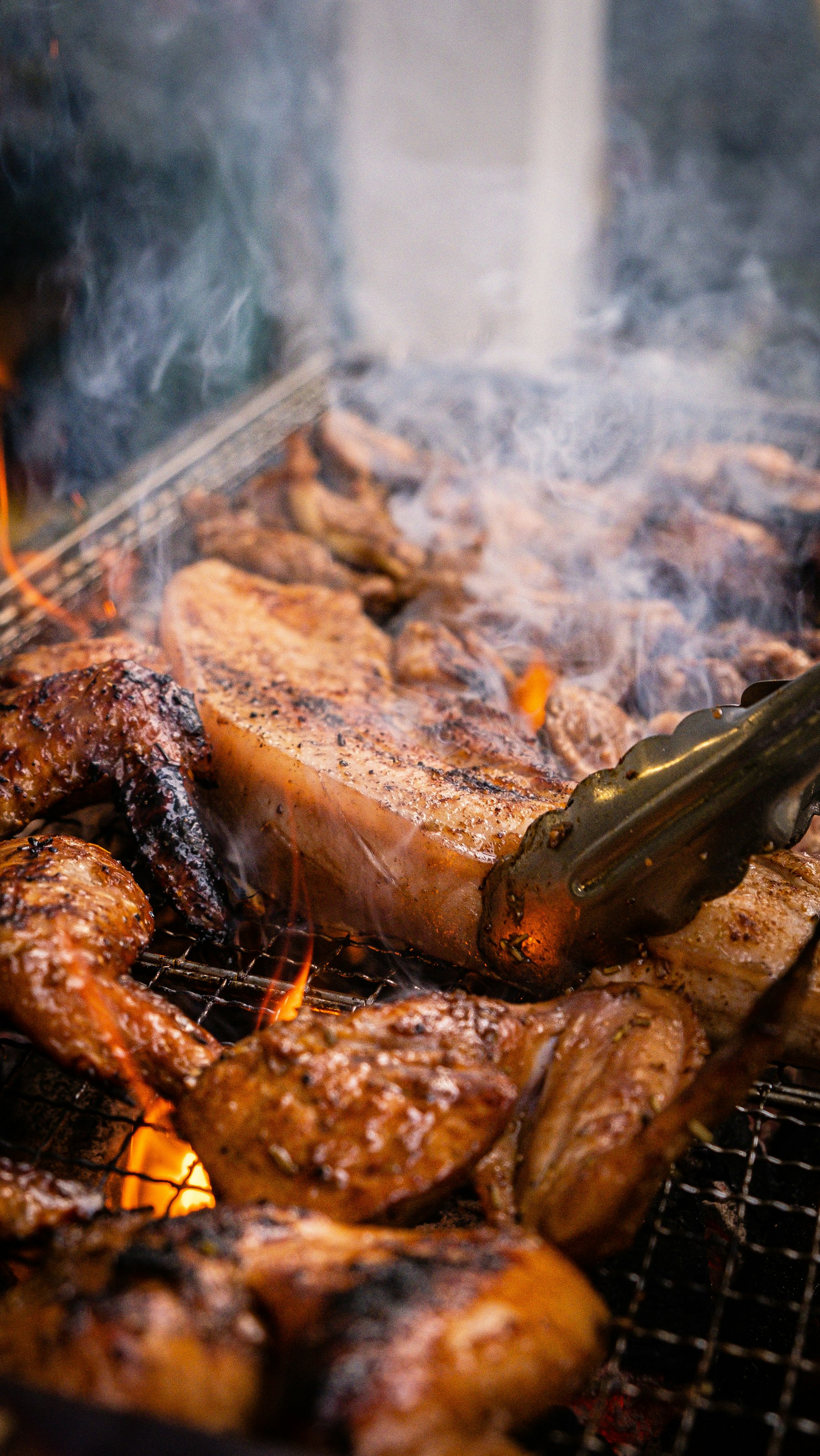 豚バラ肉が炎と煙の立つ熾火のそばで焼かれている様子
